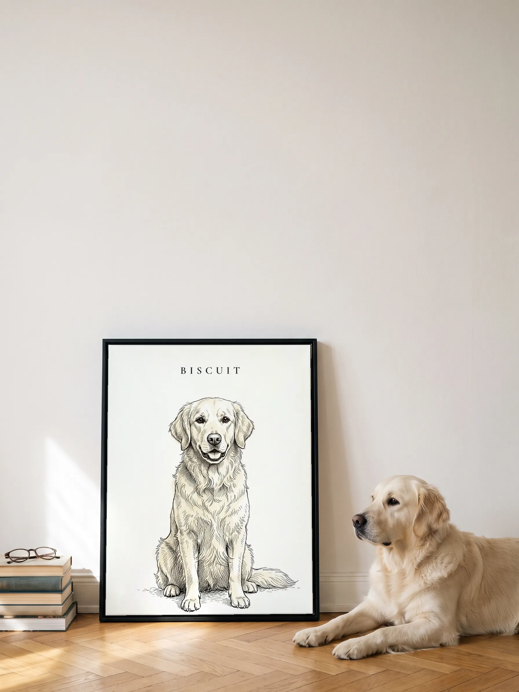 A golden retriever lying beside its own ink portrait, looking at it: a canvas in a slim black frame leaning on a white wall
