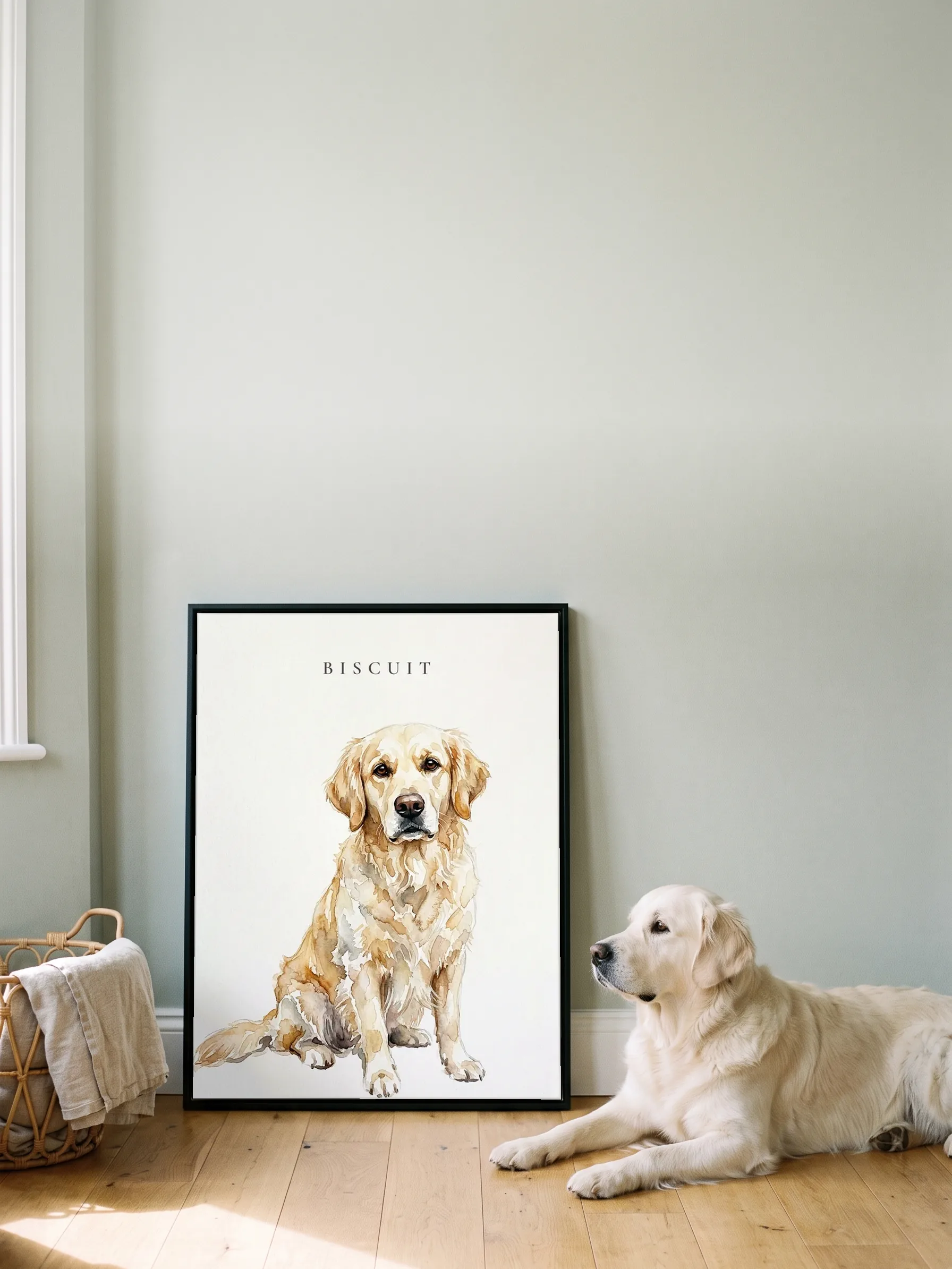 A golden retriever lying in profile beside its own watercolor portrait: a canvas in a slim black frame leaning on a sage wall, sun on the floorboards
