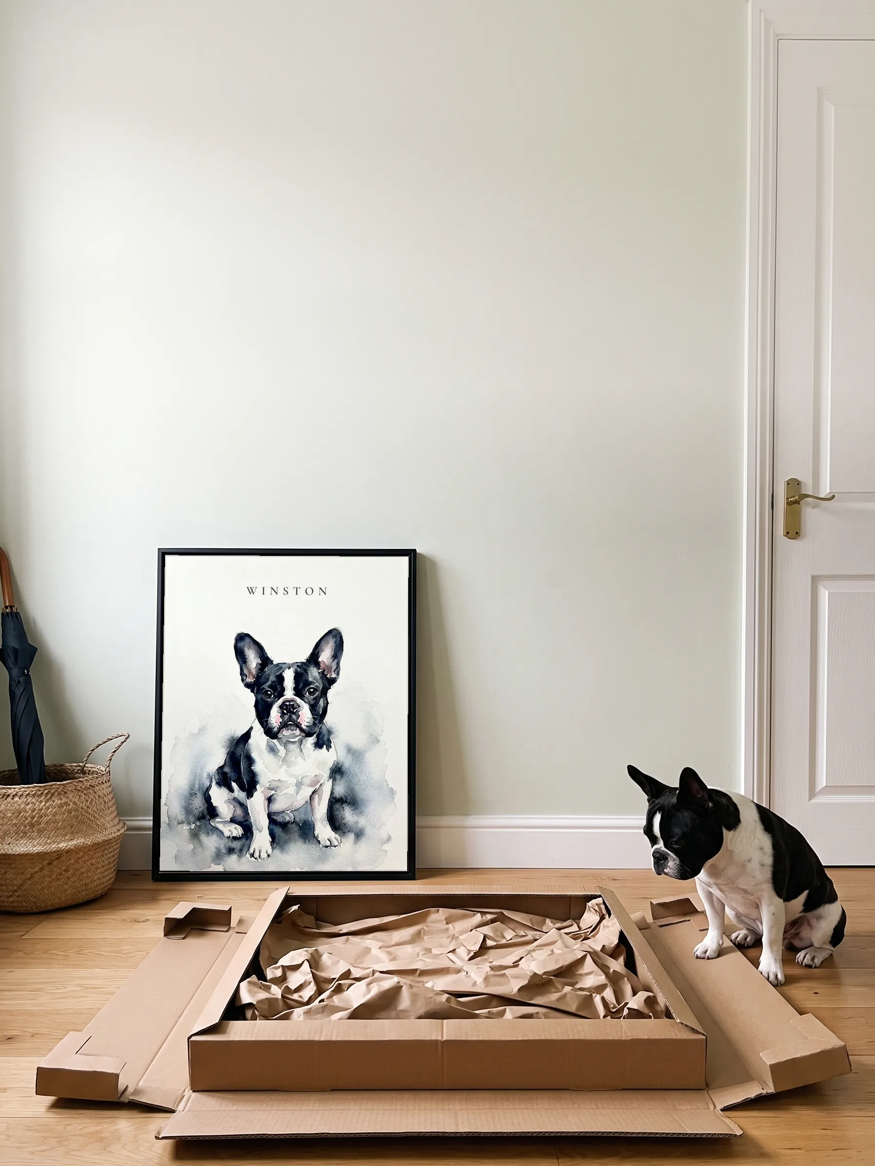 A black and white French bulldog sitting beside the open flat carton its framed canvas portrait came in; the portrait leans on the wall by the front door